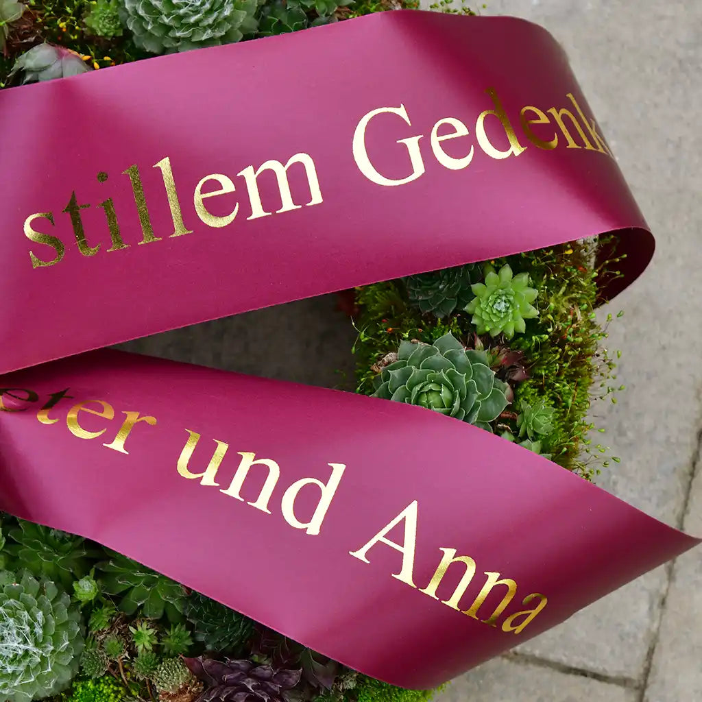 großer Trauerkranz mit Sukkulenten und roter Schleife zu Beerdigung